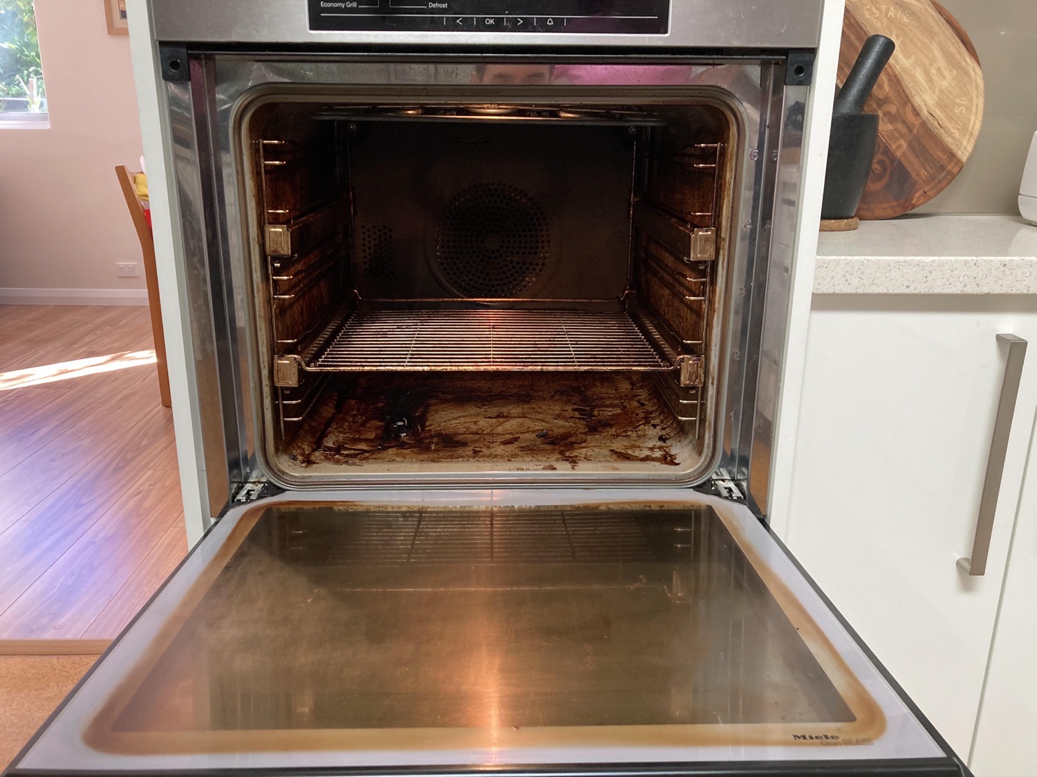 Miele wall oven before cleaning, with baked-on grease across the base and door glass
